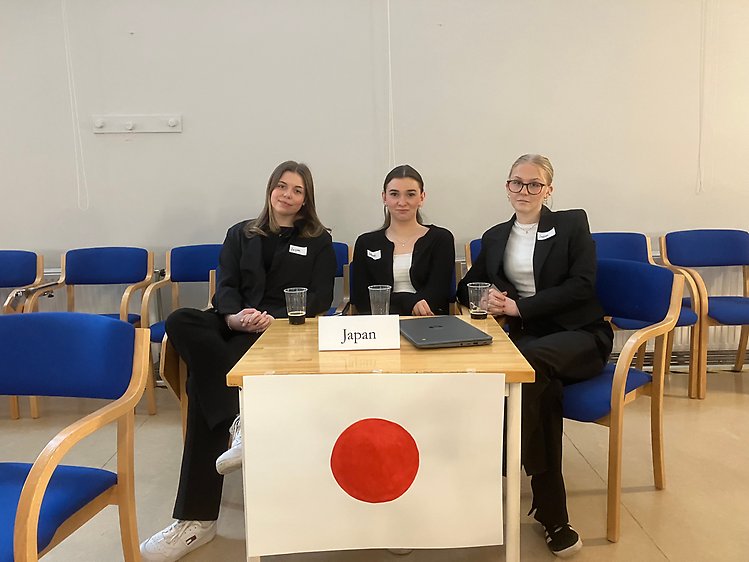 Tre elever vid ett bord med Japans flagga.